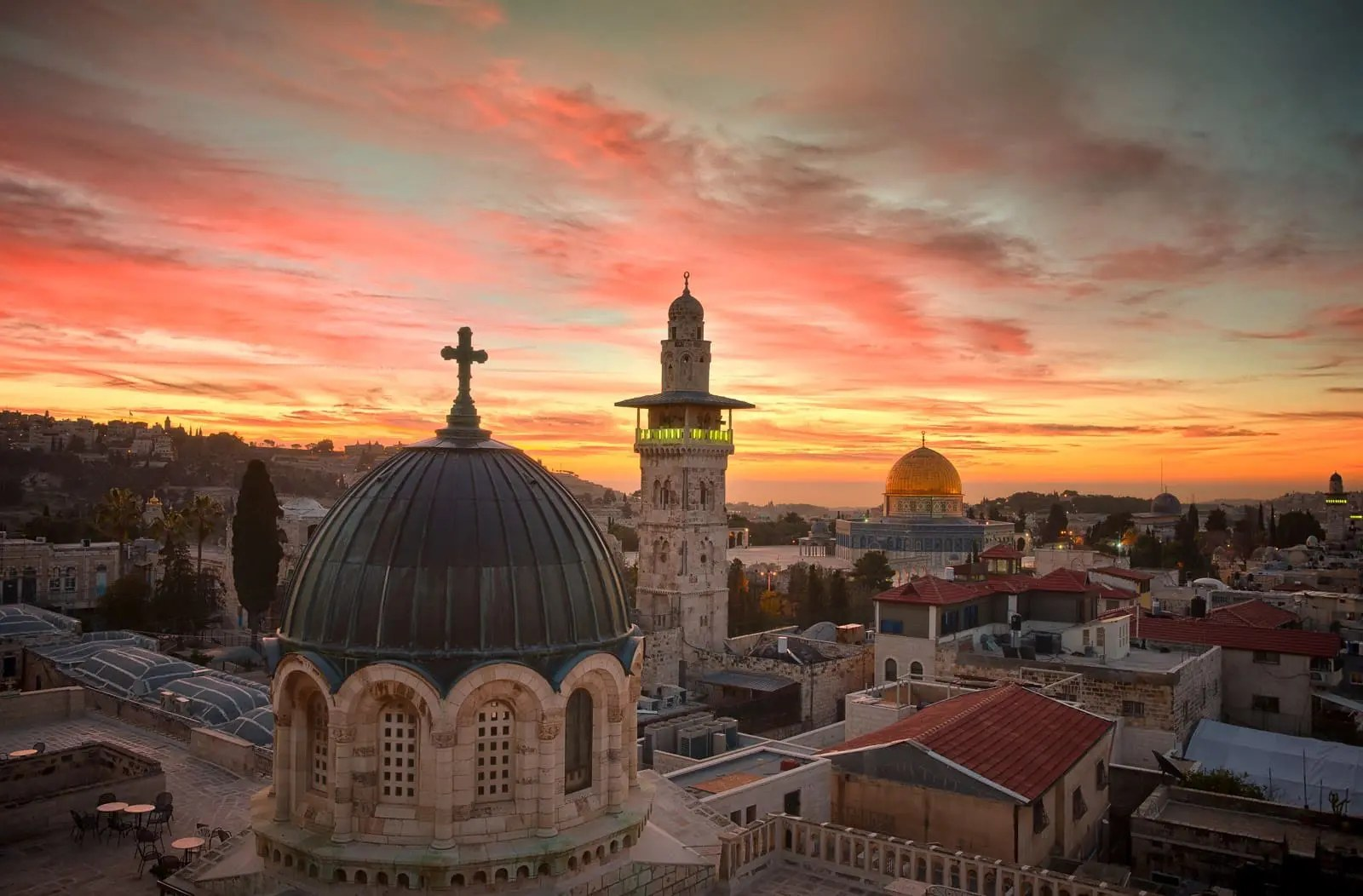 The Old City of Jerusalem at sunset, with a church dome and cross, a minaret and the Dome of the Rock